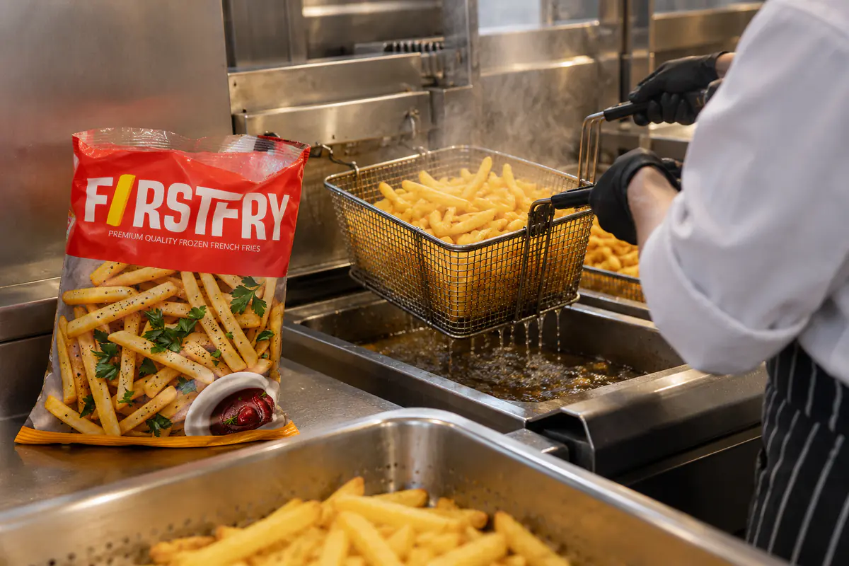 A cook lifting a basket of fries from a fryer beside an open FirstFry pack