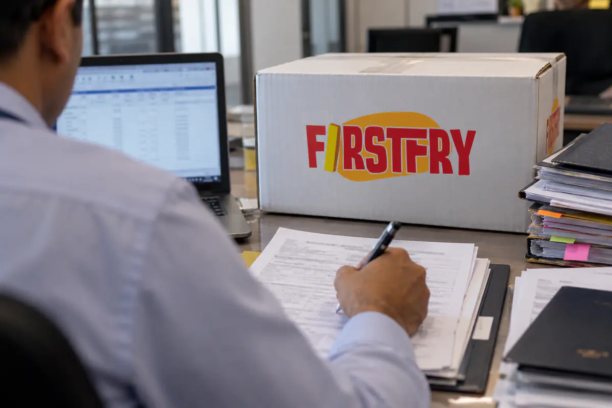 A customs broker at a desk with paper files and a FirstFry sample carton