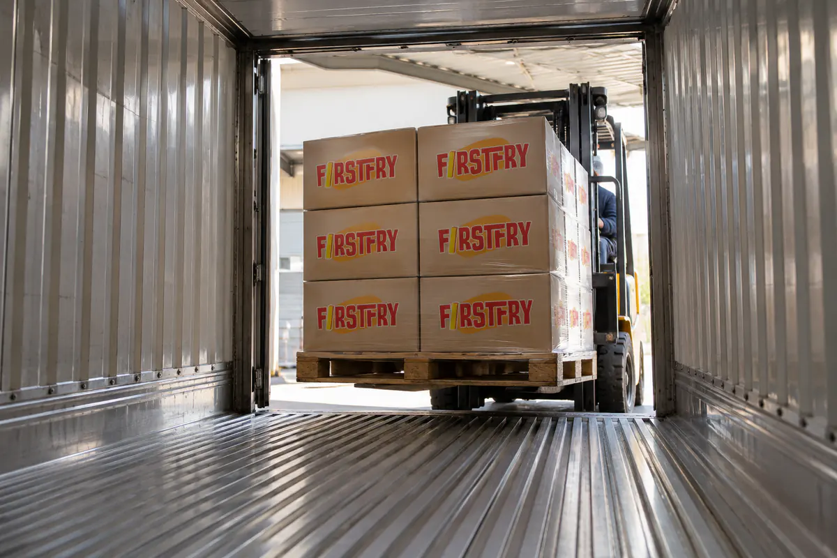 A forklift bringing FirstFry cartons onto the T-bar floor of an empty refrigerated container